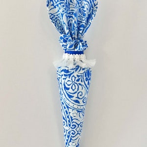K&ouml;nnte beinhalten: Eine blaue und wei&szlig;e Stoffkarotte mit Hasenohren. Die Karotte ist mit einem wei&szlig;en Quast und einem blauen Band verziert.