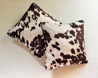 May include: Two brown and white cowhide patterned throw pillows.