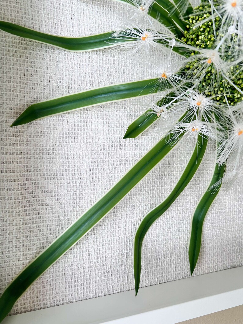 May include: A white and green floral arrangement with white feathery flowers and green leaves against a white textured background.