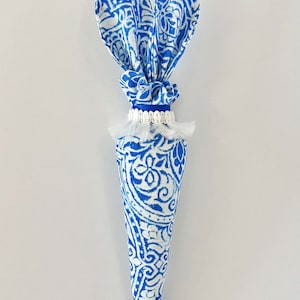 Peut inclure: Une carotte en tissu bleu et blanc avec des oreilles de lapin. La carotte est d&eacute;cor&eacute;e d'un pompon blanc et d'un ruban bleu.