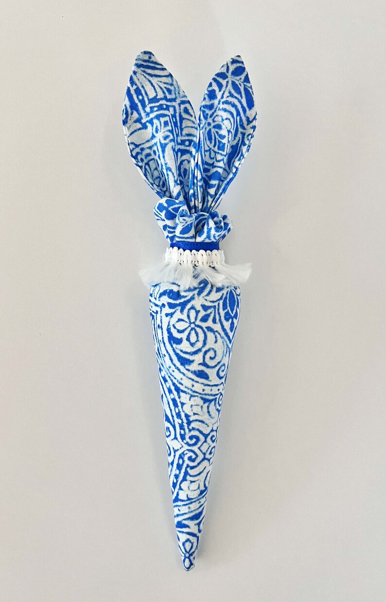 Peut inclure: Une carotte en tissu bleu et blanc avec des oreilles de lapin. La carotte est d&eacute;cor&eacute;e d'un pompon blanc et d'un ruban bleu.