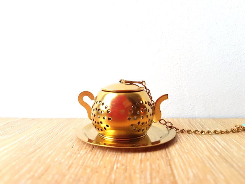 Peut inclure: Infuseur &agrave; th&eacute; en forme de th&eacute;i&egrave;re dor&eacute;e avec un couvercle et une cha&icirc;ne. L'infuseur repose sur une soucoupe dor&eacute;e assortie.
