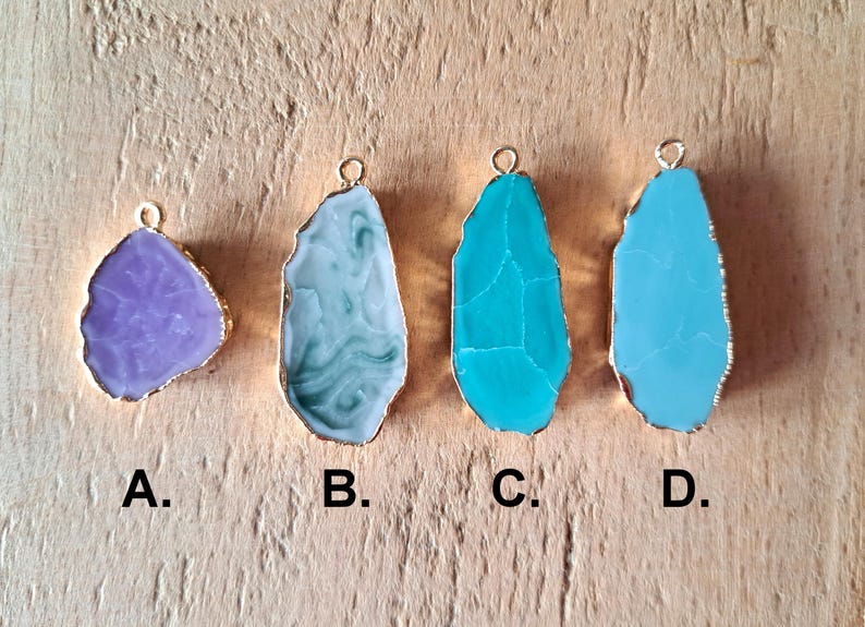 Peut inclure: Quatre pendentifs diff&eacute;rents, chacun pr&eacute;sentant une tranche d'agate unique avec une b&eacute;li&egrave;re en m&eacute;tal dor&eacute;. Les pendentifs sont &eacute;tiquet&eacute;s A, B, C et D. Le pendentif A est une agate violette claire, le pendentif B est une agate bleu clair et blanc, le pendentif C est une agate turquoise et le pendentif D est une agate bleu clair.