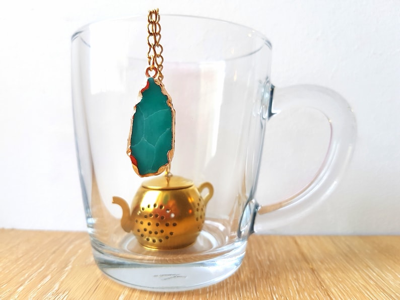 Peut inclure: Une infuseur &agrave; th&eacute; en forme de th&eacute;i&egrave;re dor&eacute;e avec un pendentif en agate verte suspendu &agrave; une cha&icirc;ne dor&eacute;e. L'infuseur est dans une tasse en verre transparent.