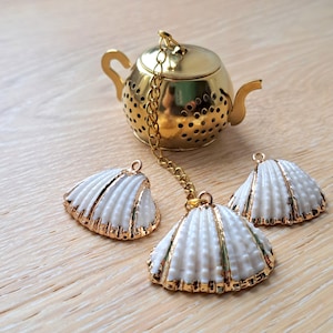 Pode incluir: Infusor de chá em forma de bule de ouro com uma corrente e três infusores de chá em forma de concha branca.