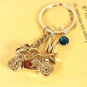 Peut inclure: Porte-clés en argent en forme de moto avec un charme en gemme bleue et un charme en lettre M argenté. Le porte-clés est attaché à un anneau de clé en argent.