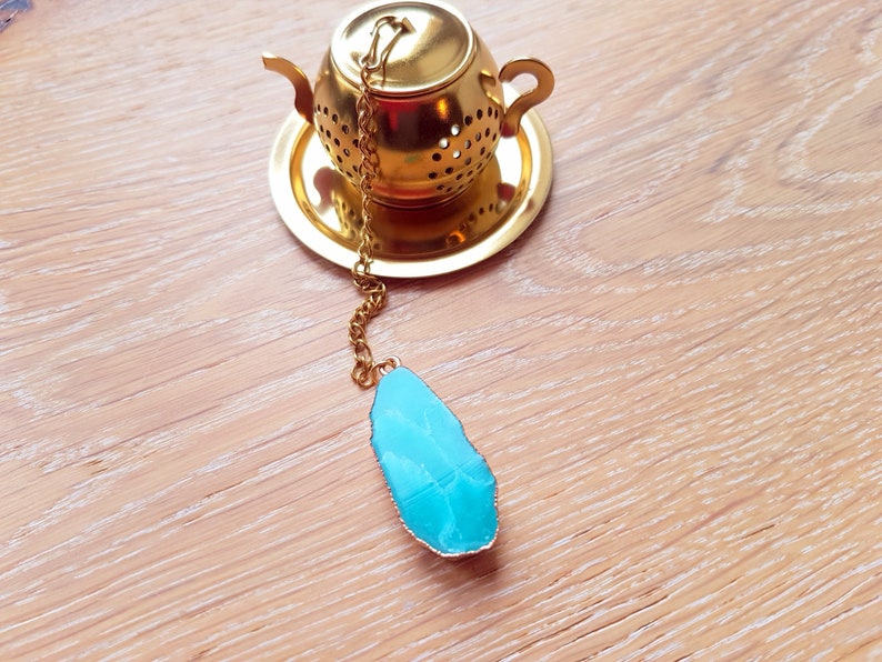 Peut inclure: Une infuseur &agrave; th&eacute; en forme de th&eacute;i&egrave;re dor&eacute;e avec une pierre pr&eacute;cieuse bleue attach&eacute;e &agrave; la cha&icirc;ne.