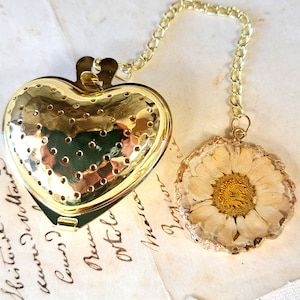 Peut inclure: Infuseur à thé en forme de cœur doré avec une chaîne et un ornement rond en fleurs pressées bordé d'or. La fleur est une marguerite blanche avec un centre jaune.