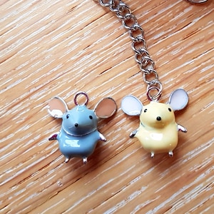 Pode incluir: Uma corrente de prata com dois pingentes de rato. Um rato é azul claro com orelhas laranja e o outro é amarelo com orelhas brancas.