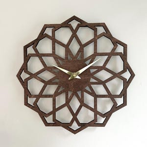 May include: A wooden wall clock with a geometric starburst design. The clock features a dark brown finish with gold-colored hands and a central hub. The intricate pattern is cut out of the wood, creating an open, airy aesthetic.