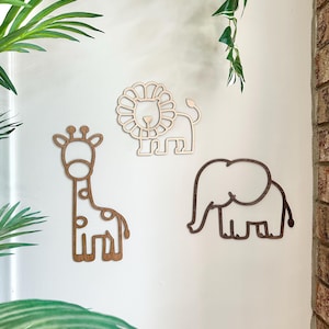 May include: Three wooden animal wall decorations: a giraffe with spots, a lion with a mane, and an elephant. The giraffe and elephant are a medium brown color, while the lion is a light tan. The decorations are mounted on a white wall.