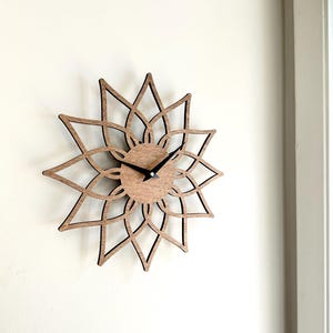 May include: A wooden wall clock with a floral design. The clock has a light brown wooden face and black clock hands. The outer frame is a dark brown, openwork design in the shape of a flower.