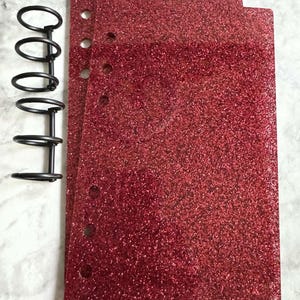 May include: Three red glitter planner pages with a black metal disc bound system.