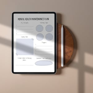 Puede incluir: Una tableta digital que muestra un plan de mantenimiento de la salud mental con secciones para enumerar las fortalezas, las se&ntilde;ales de advertencia, las estrategias de afrontamiento, los desencadenantes y las personas a las que acudir. La tableta est&aacute; sobre una superficie de madera con un l&aacute;piz &oacute;ptico al lado.