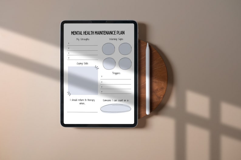 Puede incluir: Una tableta digital que muestra un plan de mantenimiento de la salud mental con secciones para enumerar las fortalezas, las se&ntilde;ales de advertencia, las estrategias de afrontamiento, los desencadenantes y las personas a las que acudir. La tableta est&aacute; sobre una superficie de madera con un l&aacute;piz &oacute;ptico al lado.