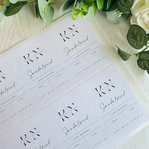 Könnte beinhalten: Fünf weiße quadratische Etiketten mit schwarzem Text. Jedes Etikett zeigt den Text "RN Kimberly Nguyen" und "Sandalwood" mit den Details "100% Natürlich", "150g" und "7 oz Sojawachskerze".