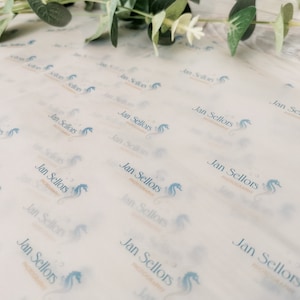 May include: White tissue paper with a repeating pattern of the text "Jan Sellors PHOTOGRAPHY" and a seahorse logo in light blue. Greenery is visible in the upper right corner. The paper is slightly translucent.