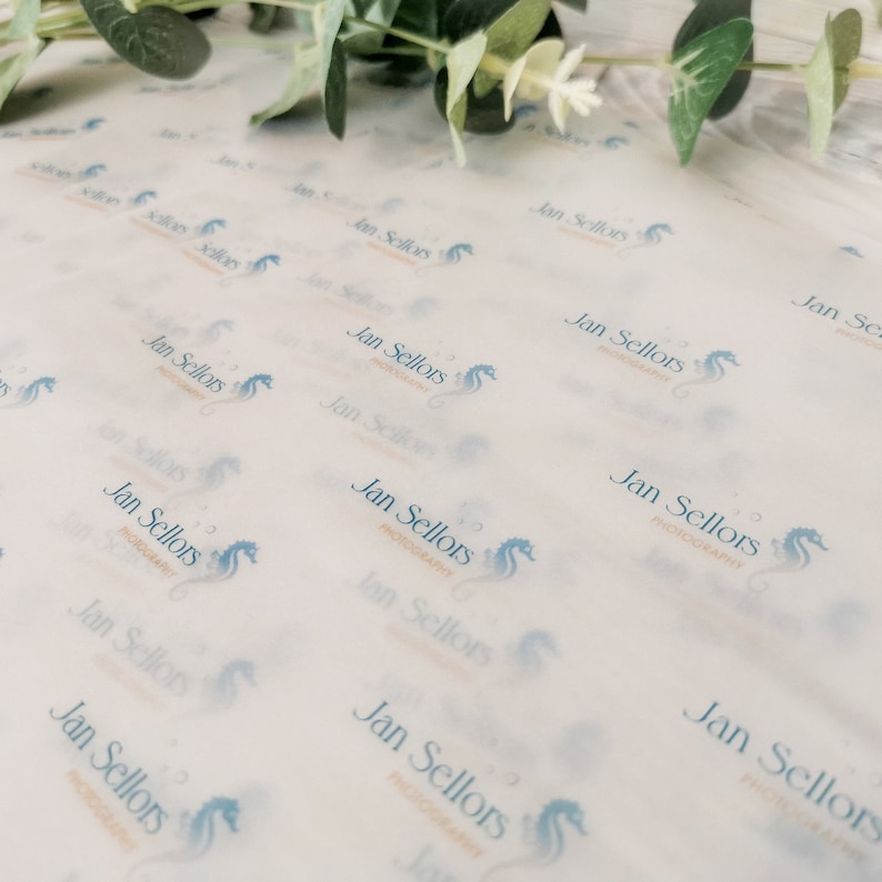 May include: White tissue paper with a repeating pattern of the text "Jan Sellors PHOTOGRAPHY" and a seahorse logo in light blue. Greenery is visible in the upper right corner. The paper is slightly translucent.