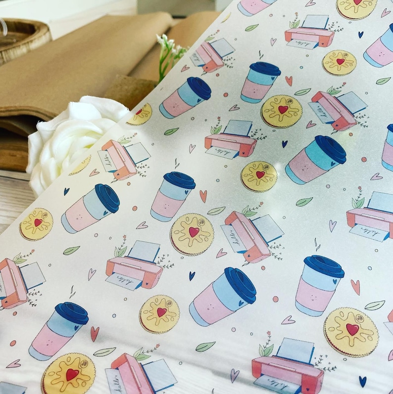 May include: White wrapping paper with a repeating pattern of pink and blue coffee cups, pink printers, and yellow heart-shaped cookies. Small green leaves and blue hearts are scattered throughout the design. The word "hello" is printed on the printer paper.