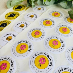May include: A sheet of white sticker paper with round, yellow and white stickers. The stickers feature a cartoon donut with legs and the text "Big Bite Donuts" and "Delicious Donuts".