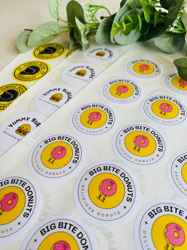 May include: A sheet of white sticker paper with round, yellow and white stickers. The stickers feature a cartoon donut with legs and the text "Big Bite Donuts" and "Delicious Donuts".