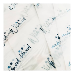 May include: White tissue paper with a repeating pattern of the word "Wildwood" in a handwritten font, along with the text "Signs & Home Decor". The design includes blue dots and stars.