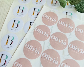 May include: Two sheets of round stickers. One sheet has white stickers with a black and green letter B and the text "Ben Dantzon Photographer". The other sheet has pink stickers with the text "Olivia Beauty Blogger" in white.