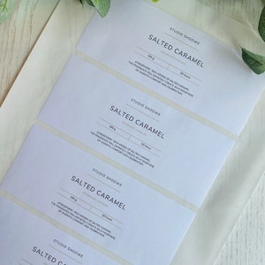 May include: Four white labels with black text for Studio Shodwe Salted Caramel homemade candles. Each label features the product name, weight (185g), burn time (50 hours), and a description of the fragrance. The labels are arranged in a stack, with the top label partially obscured by the label below it.