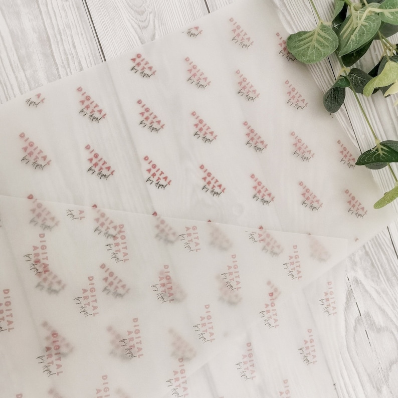 May include: Two sheets of translucent white tissue paper with a repeating pattern of the text "DIGITAL ART by Rachel" in red and black. The paper is slightly crumpled, with a wooden background.