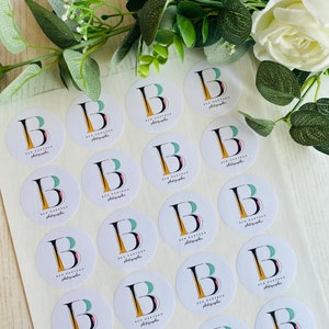 Op de afbeelding: Een vel met witte ronde stickers met een zwarte letter B, een geel en roze ontwerp en de tekst "Ben Dantzon Photographer" die op elke sticker wordt herhaald.