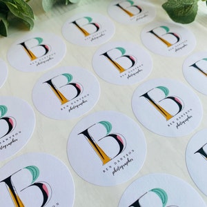 Op de afbeelding: Een vel met ronde witte stickers met een zwart en geel letter B logo en de tekst "BEN DANYSON fotograaf" gedrukt op elke sticker.