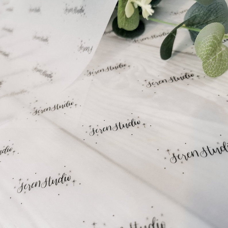 May include: White tissue paper with the text "Seren Studio" in a delicate script, repeated across the surface. Small star-like accents are scattered around the text, creating a subtle, elegant pattern.