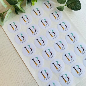Op de afbeelding: Een vel wit stickerpapier met 25 ronde stickers. Elke sticker heeft een logo met de tekst "Ben Partington Photographer" en een gestileerde letter "B" met een groen, roze en geel ontwerp.
