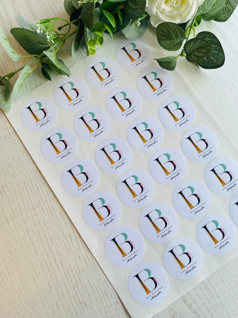 Op de afbeelding: Een vel wit stickerpapier met 25 ronde stickers. Elke sticker heeft een logo met de tekst "Ben Partington Photographer" en een gestileerde letter "B" met een groen, roze en geel ontwerp.