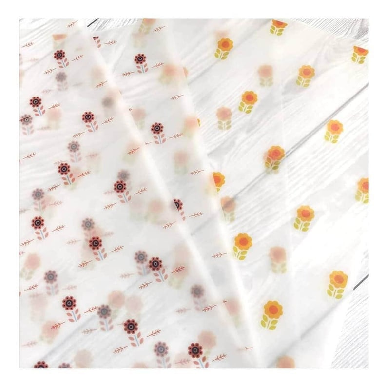 May include: White floral patterned tissue paper. The paper features a repeating pattern of stylized flowers in shades of orange, red, and brown, with green leaves. The paper is translucent and appears to be folded.