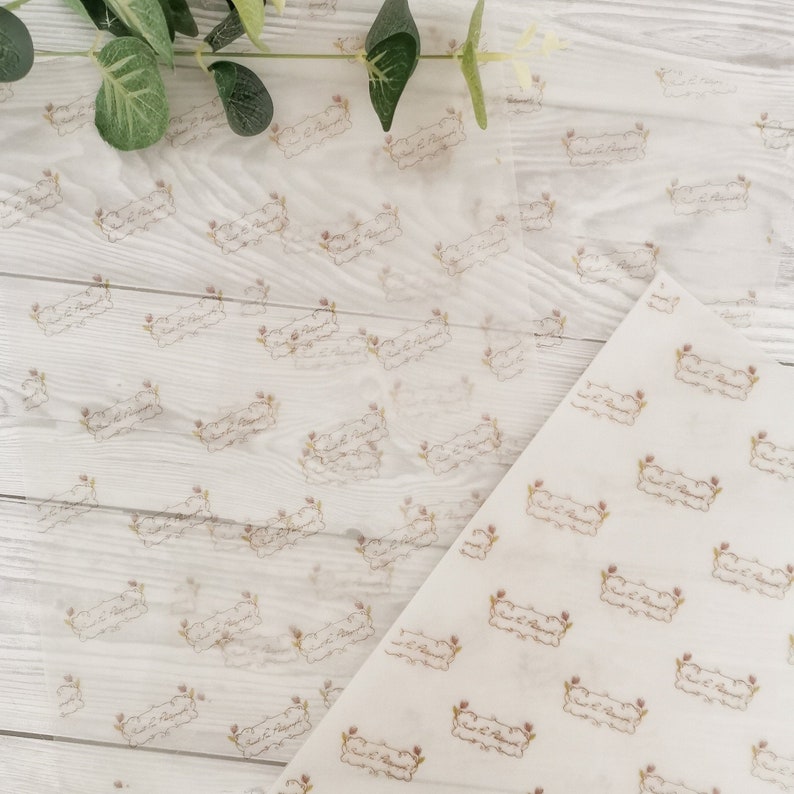 May include: Translucent white tissue paper with a repeating pattern of a decorative banner with the text "Sweet & Polished" in a script font. The banner is framed by floral elements in a light brown color.