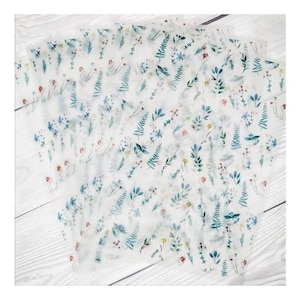 May include: Several sheets of translucent paper are arranged on a white wooden surface. Each sheet is decorated with a delicate floral pattern in shades of blue, green, red, and yellow. The design features various flowers and foliage.