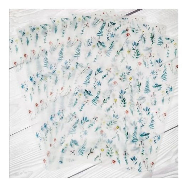 May include: Several sheets of translucent paper are arranged on a white wooden surface. Each sheet is decorated with a delicate floral pattern in shades of blue, green, red, and yellow. The design features various flowers and foliage.