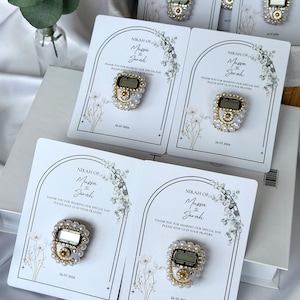 Personalized Islamic wedding favor featuring a digital tasbih counter attached to a custom Nikkah card with couple names and wedding date, elegant Muslim wedding guest gift display with floral design.