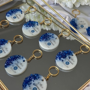 May include: A set of six white round keychains with blue glitter and a blue evil eye charm. Each keychain has the text "Ali's Sunnah" and the date "11.12.24".