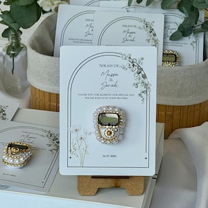 Personalized Islamic wedding favor featuring a digital tasbih counter attached to a custom Nikkah card with couple names and wedding date, elegant Muslim wedding guest gift display with floral design.