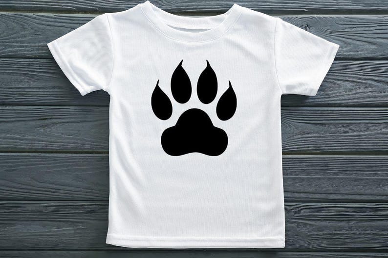 May include: A white short-sleeved t-shirt featuring a large, solid black paw print graphic centered on the chest. The garment has a classic crew neckline and a straight hem, showcasing a simple design with a bold, high-contrast animal motif.
