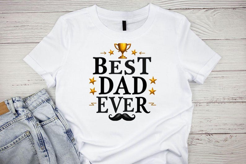May include: White t-shirt with the text "BEST DAD EVER" in black, gold, and yellow. The design includes a gold trophy, gold stars, and a black mustache. The shirt is paired with blue jeans.