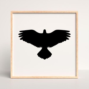 May include: A square wall art piece featuring a solid black silhouette of a bird with wings fully spread in flight, centered on a white background and enclosed within a light-toned wooden frame with a clean, simple border design.