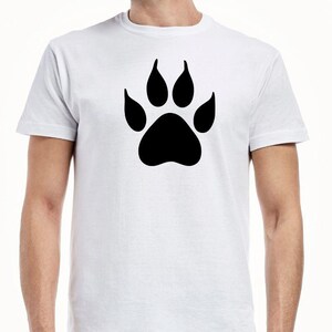 May include: A white short-sleeved t-shirt featuring a large, solid black animal paw print graphic centered on the chest. The garment has a classic crew neckline and a standard fit, showcasing a simple design with a bold, high-contrast black print.