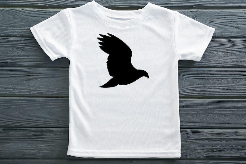 May include: A white short-sleeved t-shirt featuring a solid black silhouette of a bird in flight centered on the chest. The garment has a crew neckline and a standard fit, showcasing a clean contrast between the dark graphic and the light fabric.
