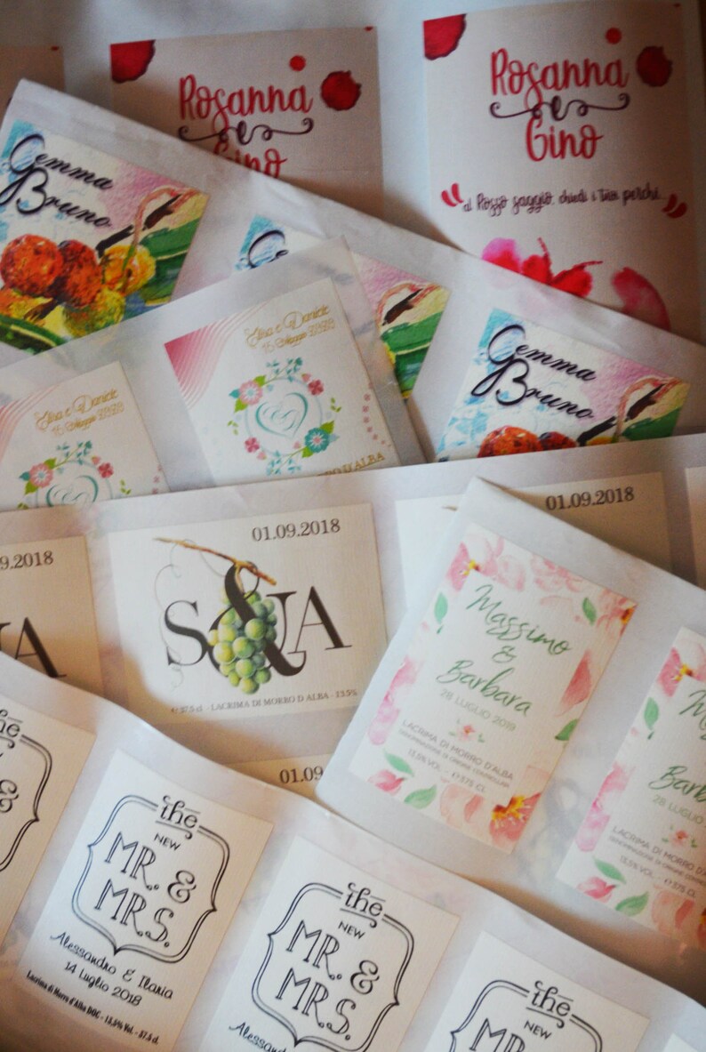May include: A collection of wedding favor labels with various designs. The labels feature floral patterns, grapes, and text in Italian. Some labels include the names of the couples and the date of their wedding.