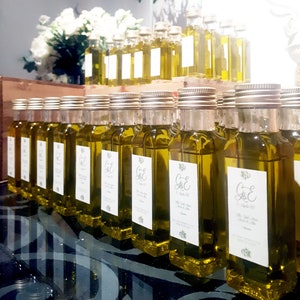 May include: A display of small glass bottles filled with olive oil, each with a personalized label featuring the initials "G&E" and the date "September 2023".