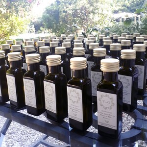 May include: A collection of small glass bottles with olive oil, each with a personalized label featuring a monogram and the text "T.G. 2023 Villa Sant'Anna Extra Virgin Olive Oil".