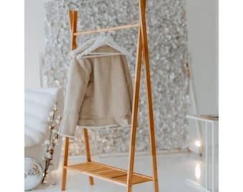 May include: A wooden clothes rack with a shelf. The rack is made of natural bamboo and has a simple, modern design. It features a single horizontal bar for hanging clothes and a lower shelf for storage.